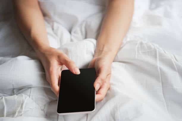 Person holding an iPhone in bed with the display turned off, no always-on screen enabled