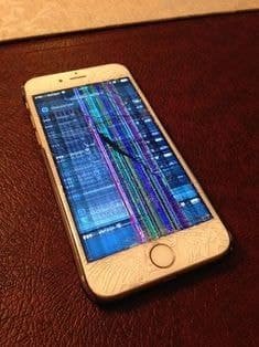 Older iPhone with shattered glass and vertical RGB lines across a dimmed screen